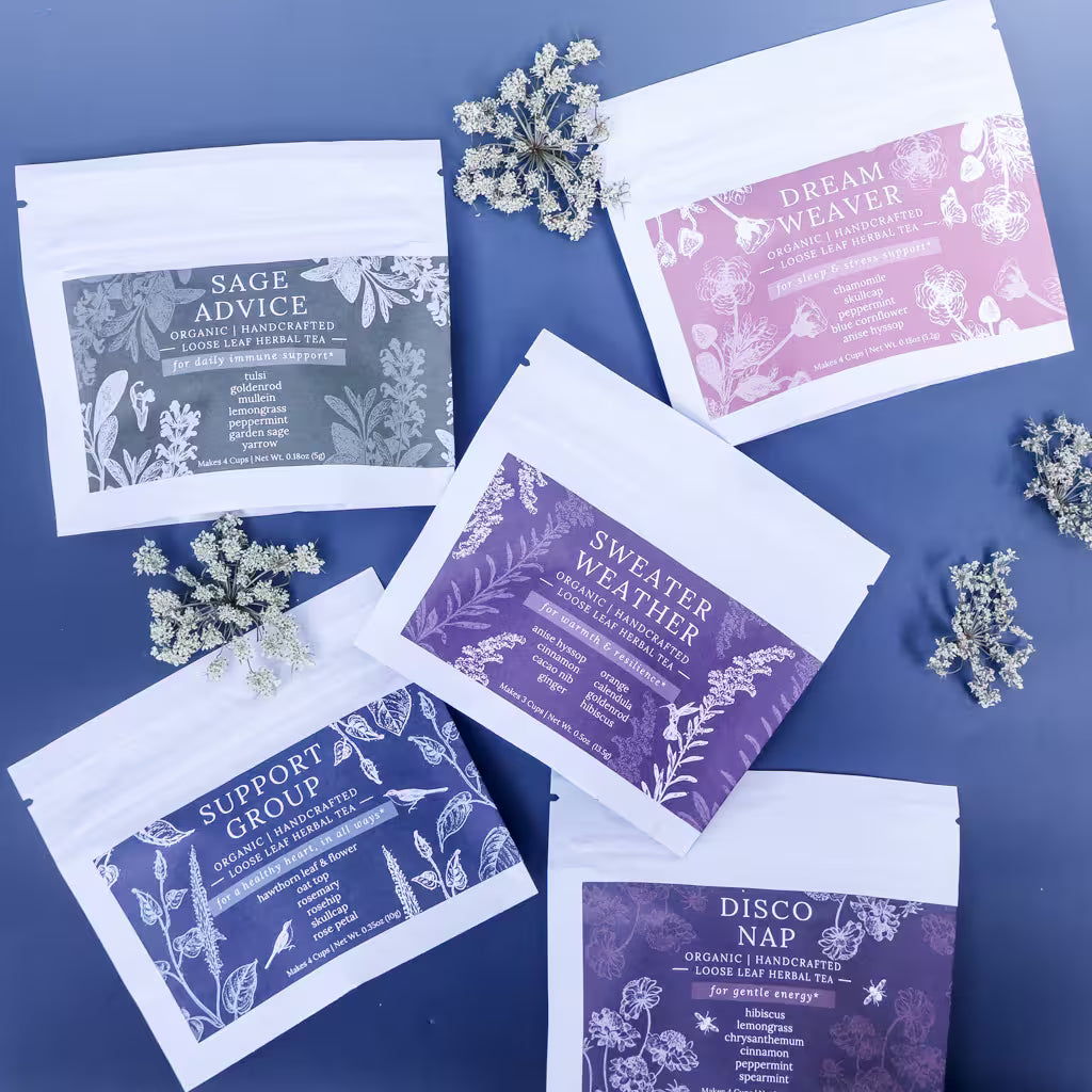 five loose-leaf herbal tea sampler bags of different tea blends with dried flowers as decoration against a blue background
