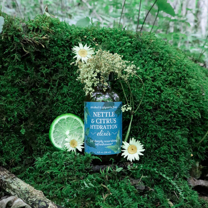 Nettle & Citrus Hydration Elixir bottle with flowers and a lime on a mossy background